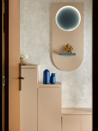 Foyer with arched beige panel, backlit circular mirror, brass idol, and blue vases on cabinet.