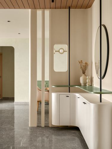 Curved beige console with green glass top beside round mirror in a softly lit foyer