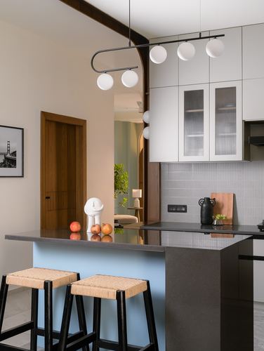 Kitchen island with pale blue base, dark stone counter, cane stools, and globe pendant light.