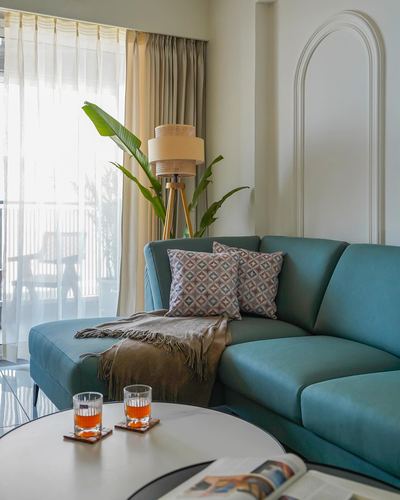 Teal sectional sofa with cushions beside arched niche and tripod lamp, sheer curtains lit by daylight