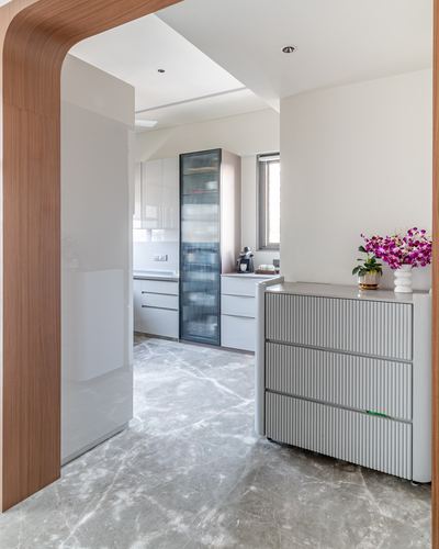 Foyer with curved wood archway, fluted grey cabinet, orchids, and marble flooring leading to kitchen