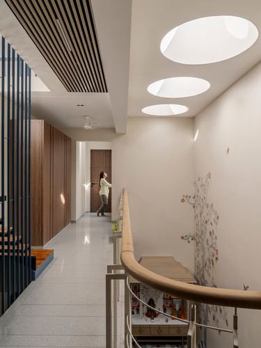 Woman stands in narrow hallway lit by three oval skylights beside a wall mural and curved staircase