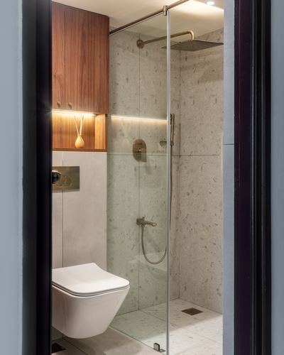 Compact bathroom with stone shower wall, brass fixtures, and walnut cabinetry seen through open door