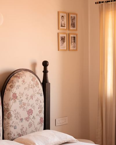 Arched floral headboard with turned wooden post beside wall of family photographs in warm-lit bedroom