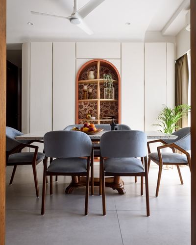 Dining room with blue velvet chairs around a round table, arched floral-wallpapered niche behind