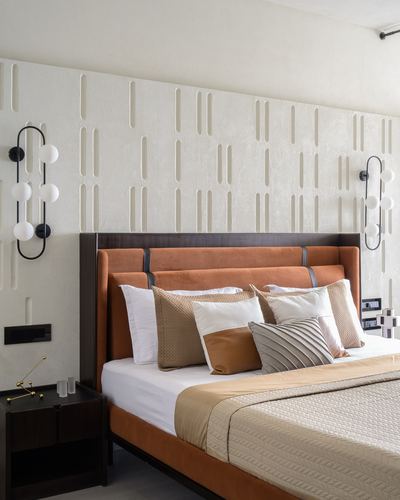 Bedroom with textured plaster wall, dark wood headboard, rust upholstery, and sculptural globe sconces