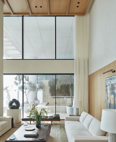 Double-height living room with floor-to-ceiling glass wall overlooking a courtyard with palms