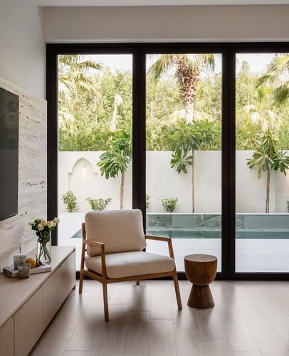 Minimalist living room with wood armchair facing glass doors overlooking a pool and palm trees