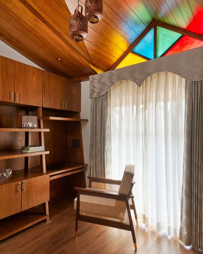 Wood-panelled study corner with cane armchair, ladder bookshelf, and triangular stained-glass gable window.