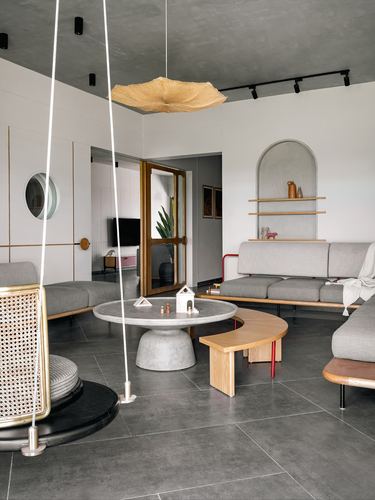 Living room with hanging cane swing, round stone coffee table, and grey sofas under an arched niche