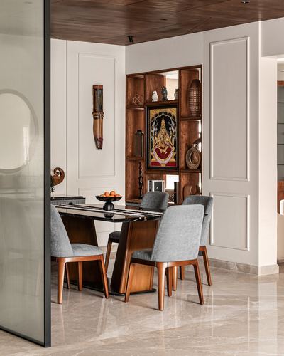 Dining area with marble table, grey velvet chairs, and a wooden display niche with artwork