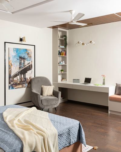 Bedroom with bed, grey armchair, built-in shelving and study desk, cityscape artwork on wall
