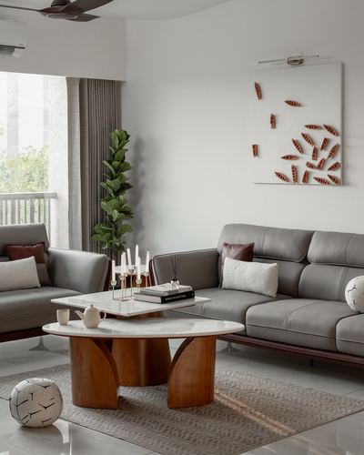 Minimalist living room with grey leather sofas, wooden sculptural coffee table, and leaf-motif wall art