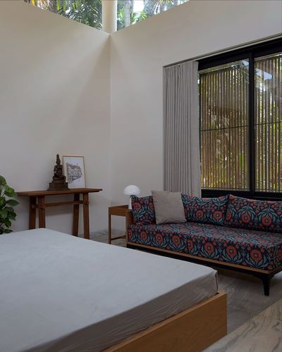 Bedroom corner with printed daybed sofa, console table, and tall window framing greenery under a double-height cutout.