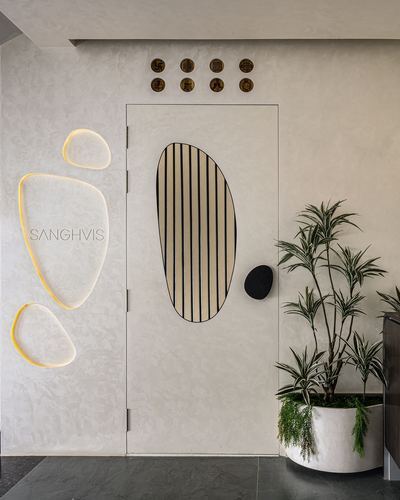 Foyer with textured white wall, organic pebble light fixtures, fluted door panel, and potted plant beside dark stone flooring