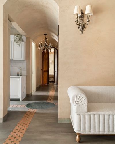 Barrel-vaulted hallway with crystal chandelier, inlaid stone floor, and linen sofa opening to kitchen