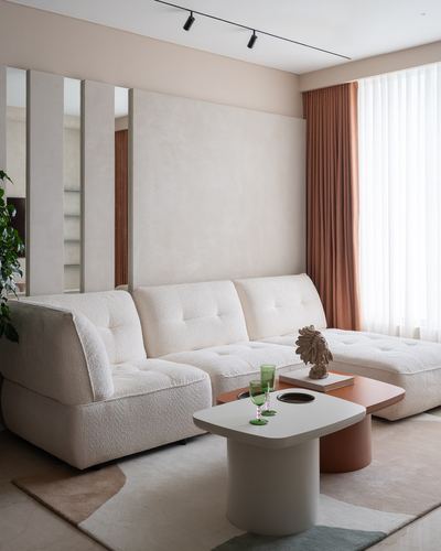 Cream boucle sectional sofa with round two-tone coffee table beside terracotta curtains