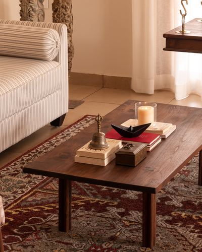 Wooden coffee table with candle, bell, and books on patterned rug beside striped sofa