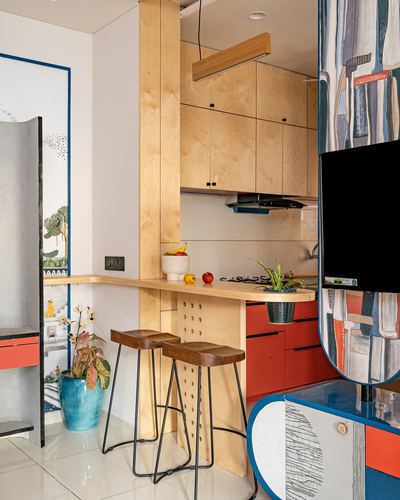 Small plywood kitchen with terracotta cabinets, breakfast counter, hairpin stools, and colorful tv backdrop