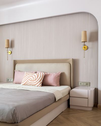 Bedroom with fluted beige headboard wall, brass sconces, and pink cushions on bed