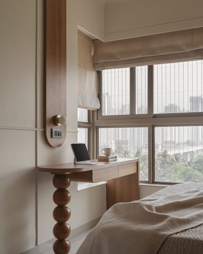 Wooden desk with stacked-sphere leg beside a window overlooking a city skyline in a beige bedroom