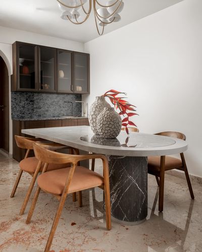 Oval marble-topped dining table with cane-backed wooden chairs beside a stone-clad wet bar