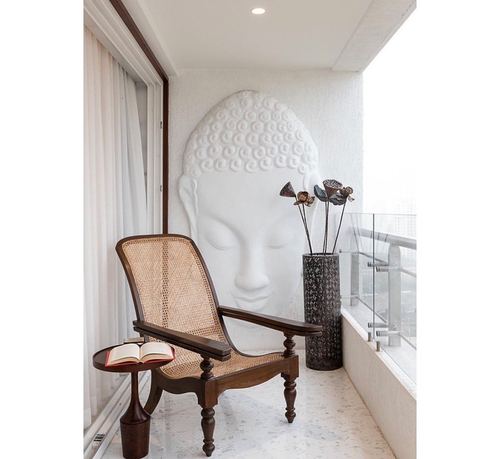 Cane armchair beside a sculpted buddha wall relief on a white balcony