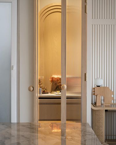 Fluted glass door with round brass pull opens onto a warm-lit arched study niche