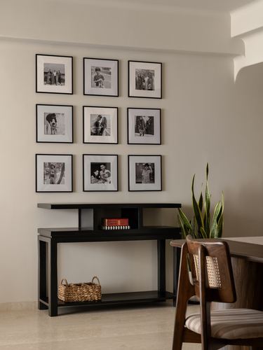 Black console table below a 3x3 black-framed photo gallery, with basket, books and plant