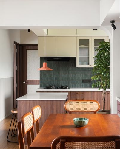 Open kitchen with green tiled backsplash, orange pendant light, wood island and cane dining chairs