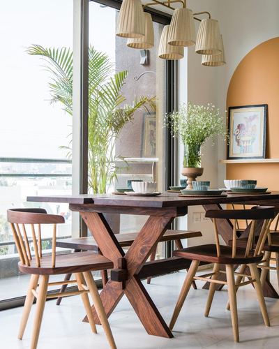Wooden dining table with spindle chairs beneath pleated pendant lights near a terracotta arched niche