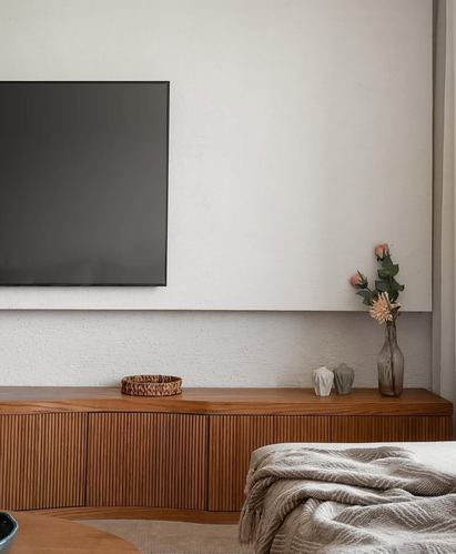 Wall-mounted tv above a fluted wood console with vase and basket, sofa with throw in foreground