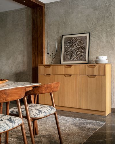 Wooden fluted sideboard with artwork and candlesticks beside a walnut dining table with patterned chairs