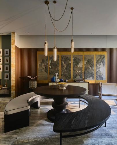 Round dark wood dining table with curved benches beneath draped pendant lights, gilt landscape screen behind