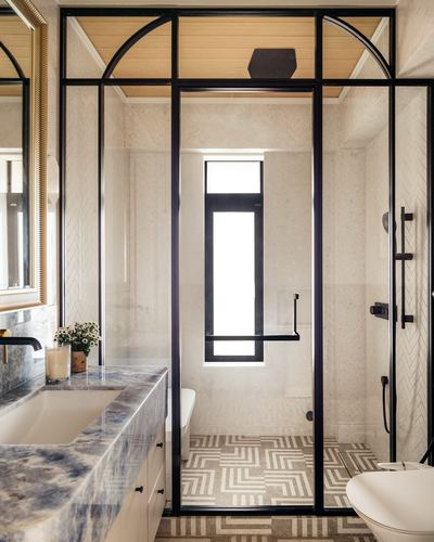 Bathroom with arched black steel glass partition, veined stone vanity, and patterned floor tile in Mumbai apartment