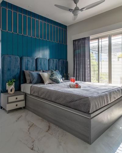 Bedroom with teal ribbed accent wall, upholstered headboard, grey bed, marble flooring, and large window.