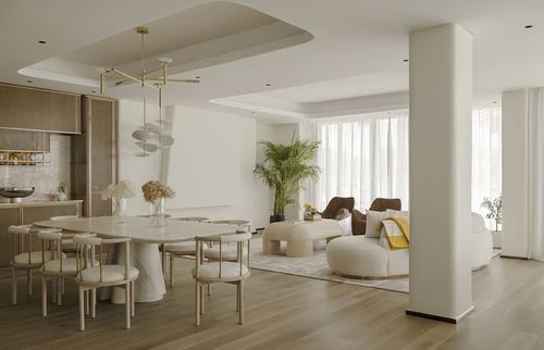 Open-plan dining and living space with marble table, brass chandelier, and wood flooring