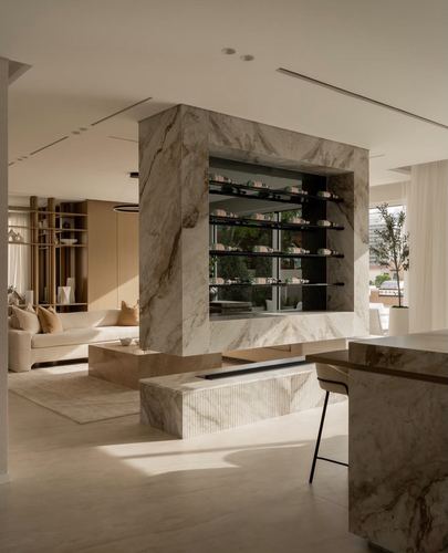 Sunlit living space with a large veined stone column housing a wine display, sofa and bar seating nearby