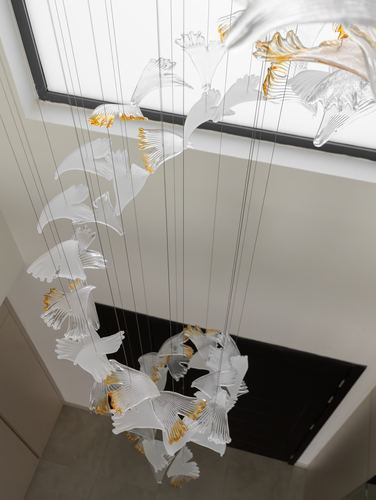 Cascading glass leaf chandelier hanging from a skylight above a stairwell