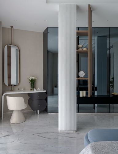 Fluted white column divides marble-floored bedroom with vanity, mirror, and mirrored passage beyond