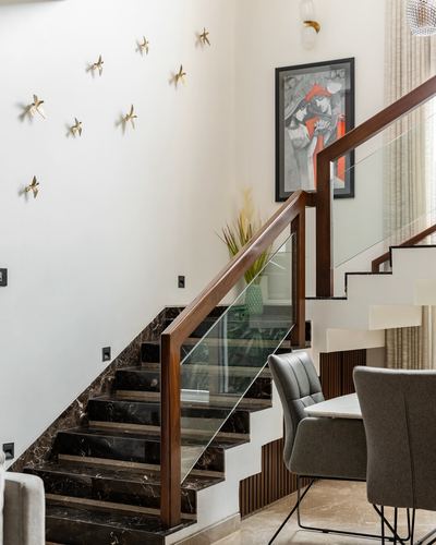 Marble staircase with wood and glass railing beside dining area in double-height foyer