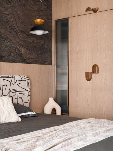 Bedroom corner with wood wardrobe, arched brass handles, dark stone wall, and graphic headboard