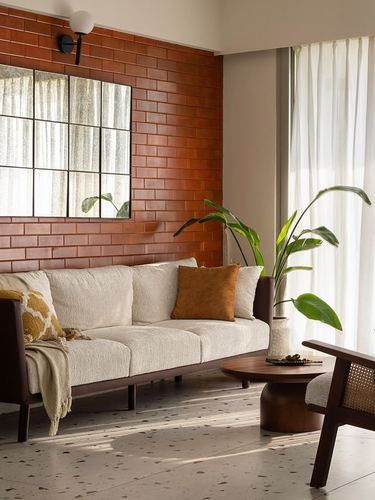 Living room corner with brick wall, cream sofa, cane armchair, and terrazzo floor in daylight