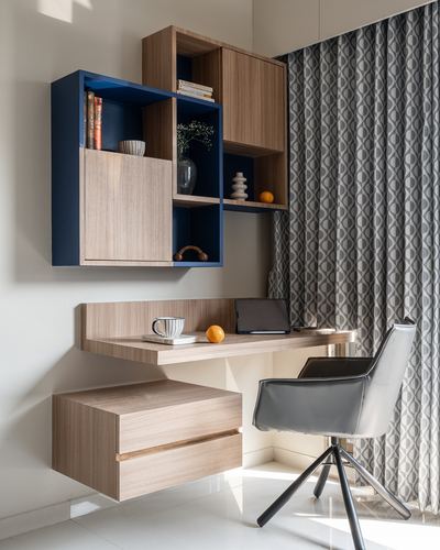 Wall-mounted wood desk and navy-backed shelving unit beside patterned curtain in study nook