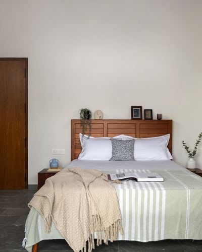 Minimalist bedroom with louvered wood headboard, sage green bedding, and stone floor