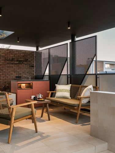 Covered terrace lounge with cane armchairs, sofa, brick tea counter and perforated metal screens
