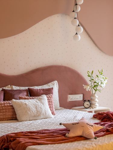 Child's bedroom with wave-shaped mauve velvet headboard, star wallpaper, and globe pendant lights
