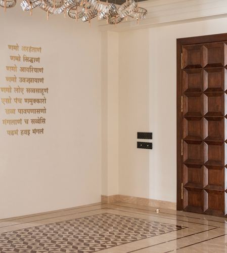Foyer with carved wooden door, patterned stone floor, and gold Jain prayer text on wall