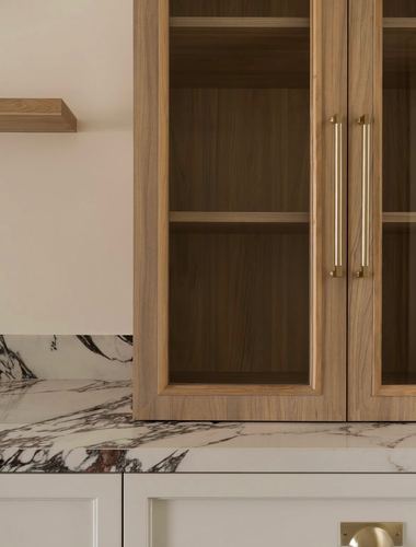 Close-up of wood glass cabinet with brass handles above veined marble counter and backsplash