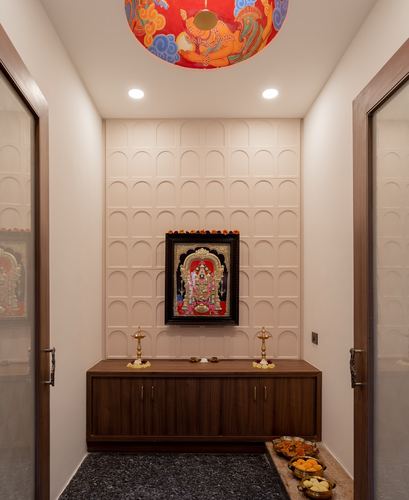 Pooja alcove with arched wall panelling, tanjore painting, and wooden console below